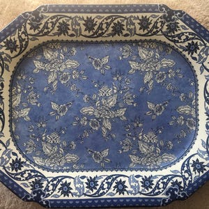 May include: A rectangular serving tray with rounded corners featuring a blue and white floral pattern. The center displays a dense arrangement of flowers, while the wide border is decorated with a continuous scrolling vine and floral motif.