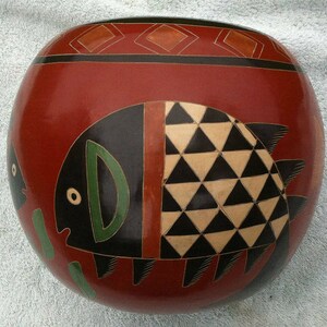 May include: A red ceramic bowl with a black and white geometric design of triangles. The bowl has a black and green fish design on the side.