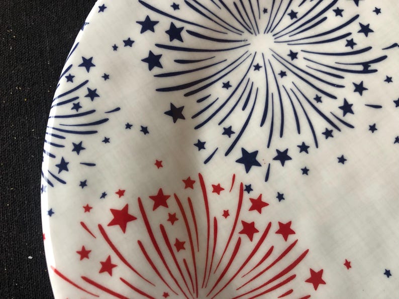 Op de afbeelding: Witte plaat met een feestelijk vuurwerkontwerp in rood en marineblauw. De plaat heeft stervormige patronen en verspreide sterren, wat een feestelijk en patriottisch thema cre&euml;ert. Perfect voor het serveren van eten op een zomerse bijeenkomst.