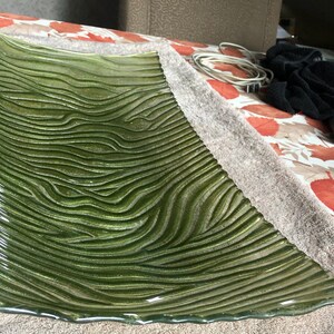 May include: A rectangular glass tray in a deep olive green hue, featuring a prominent textured surface with raised, wavy, horizontal lines that mimic the organic appearance of wood grain or flowing water across the entire piece.