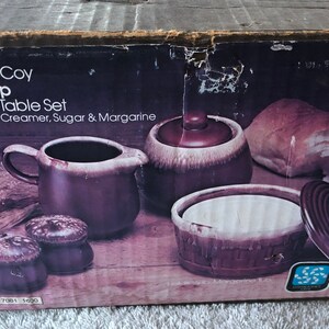 May include: A box for a Nelson McCoy Brown Drip Center of Table Set. The box shows a brown and white creamer, sugar bowl, salt and pepper shakers, and two rolls of bread. The text on the box reads "Nelson McCoy Brown Drip Center of Table Set Salt, Pepper, Creamer, Sugar & Margarine 7001 1600".