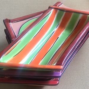 May include: A set of four ceramic serving dishes with a striped design in shades of green, orange, and brown. The dishes are stacked on top of each other.