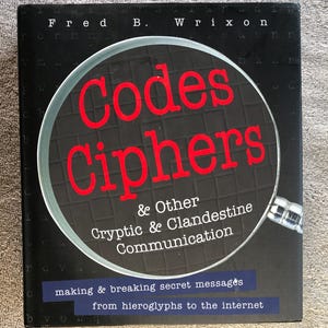 May include: A book titled "Codes Ciphers & Other Cryptic & Clandestine Communication" by Fred B. Wrixon. The title is in red, with a magnifying glass graphic. The book cover is black with white text and a blue banner at the bottom.