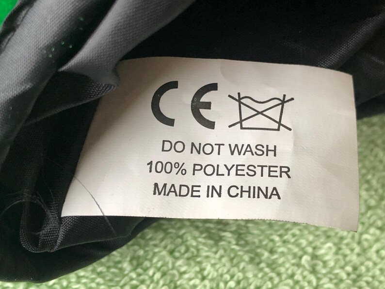 May include: A white tag with black text that reads "CE" and "Do Not Wash 100% Polyester Made in China". The tag is attached to a black fabric.