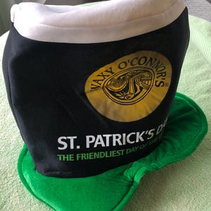 May include: A black and green felt hat shaped like a pint glass with the text "Waxy O'Connor's" and "St. Patrick's Day The Friendliest Day of the Year" printed on it.