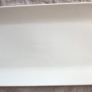 May include: A rectangular white ceramic serving platter with a smooth, glossy finish and slightly raised edges. The dish features a clean, solid white surface with no patterns or decorations, presenting a simple and functional design.