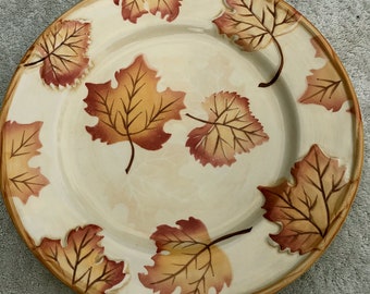 May include: A ceramic dinner plate with a cream background and a design of brown and orange leaves.
