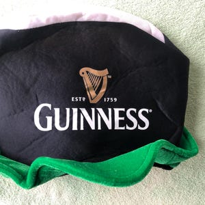 May include: Black and green Guinness hat with a white brim and a gold harp logo. The hat says "ESTD 1759 GUINNESS".