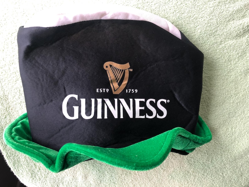 May include: Black and green Guinness hat with a white brim and a gold harp logo. The hat says "ESTD 1759 GUINNESS".