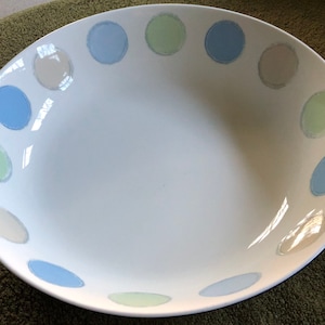 May include: White oval serving bowl with a series of pastel-colored polka dots around the rim. The dots are in shades of blue, green, and beige. The bowl has a glossy finish and is likely made of ceramic or porcelain.