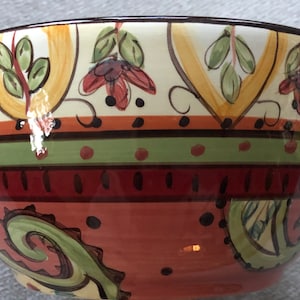 May include: A ceramic bowl with a colorful floral and paisley design. The bowl has a brown rim and is decorated with yellow, green, red, and brown colors.