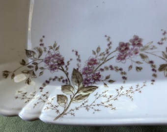 May include: A white porcelain serving tray with a floral design. The tray has a scalloped edge and features a delicate pattern of brown and pink flowers.