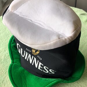 May include: A black and green Guinness hat with a white top and the text "ESTD 1759 GUINNESS" on the front.