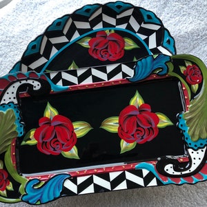 May include: A black rectangular serving tray with a decorative border featuring a black and white chevron pattern, blue and green swirls, and red roses. The tray has a raised edge and gold accents.