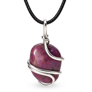 May include: A polished, deep magenta-colored gemstone pendant wrapped in silver-toned wire. The pendant is suspended from a smooth, black cord necklace. The stone has a rounded, irregular shape with visible dark inclusions and a glossy finish.