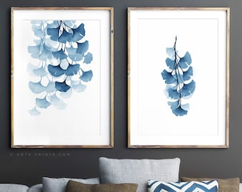 Può includere: Due stampe ad acquerello incorniciate di foglie di ginkgo blu su sfondo bianco. Le stampe sono appese a una parete grigio scuro sopra un divano grigio con cuscini a motivi blu e marroni.