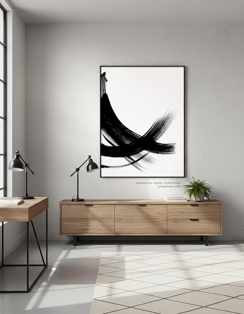 Modern minimalist black and white abstract art print with expressive bold brush strokes hanging in a Scandi-industrial home office above a wooden sideboard.
Below the artwork, there is a text: "created by Agnes Szafranska - arteprinte.com".