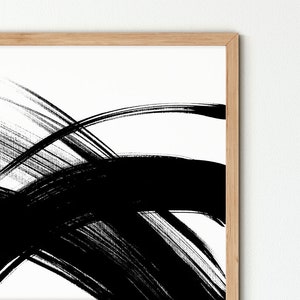 A close-up of the abstract black and white painting with bold brushstrokes in a wooden frame.