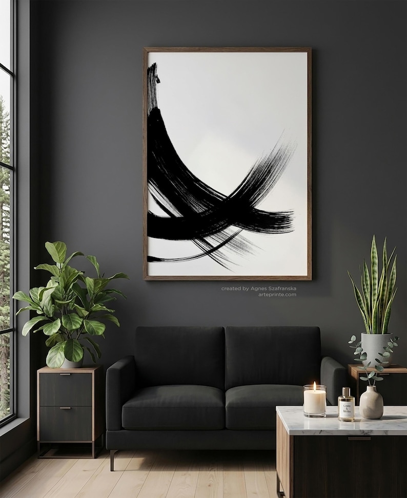 Vertical wall art in a moody dark living room featuring a large wood-framed black and white abstract brushstroke print above a black sofa. The interior includes a fiddle leaf fig, snake plant, and a marble coffee table with a candle and eucalyptus, creating a luxury modern home office atmosphere.
Below the wall art, there is a text: "created by Agnes Szafranska - arteprinte.com".