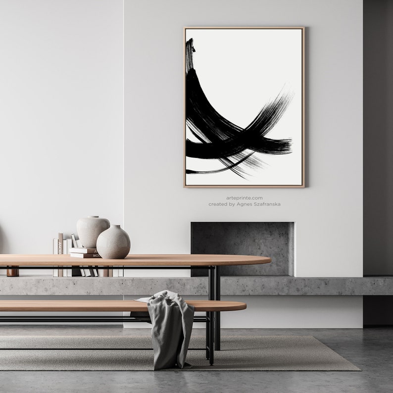 A black and white abstract painting with bold brushstrokes hangs above a wooden table and bench in a modern living room. The painting is framed.
Below the wall art, there is a text: "created by Agnes Szafranska - arteprinte.com".