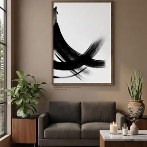 Vertical wall art in a warm mid-century modern living room featuring a large wood-framed black and white minimalist line art print above a brown sofa.
The interior includes a fiddle leaf fig, a snake plant in a rustic pot, and a marble coffee table with a candle. Large window with a pine forest view creates a bright, natural atmosphere.
Below the artwork, there is a text: "created by Agnes Szafranska - arteprinte.com".