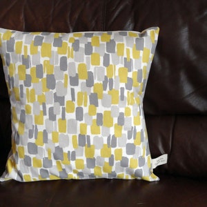 May include: A yellow and gray patterned throw pillow with a white background. The pillow has a white tag attached to it.