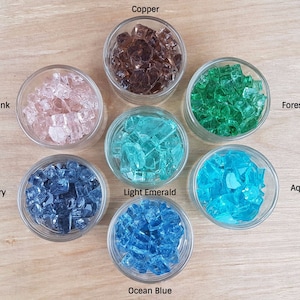 May include: Eight small glass jars filled with different colored glass pieces. The colors are peachy pink, dark ivory, light emerald, ocean blue, aqua blue, forest green, and copper.