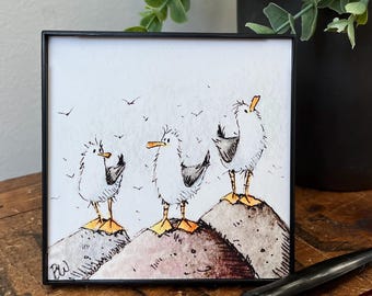 May include: A watercolor painting of three cartoon seagulls perched on rocky cliffs. The seagulls are white with black eyes and beaks, and they have orange feet. The background is a light blue watercolor wash.