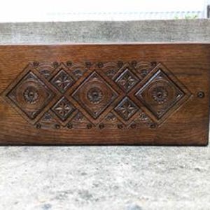 May include: A wooden box with a carved design on the front. The design features five diamond shapes with intricate details.