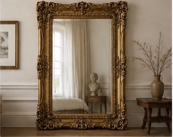 May include: A large rectangular floor mirror featuring an ornate, heavy gold-toned frame with intricate carved floral and scrollwork detailing. The reflective glass surface displays a clear view of a room interior, including a window and furniture.