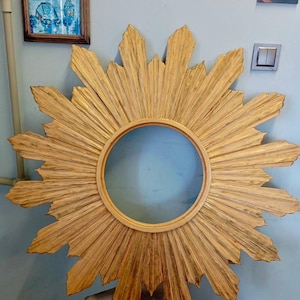 May include: A large circular mirror frame featuring a sunburst design with numerous radiating golden rays. The frame has a textured, weathered gold finish with visible dark streaks, surrounding a central circular opening for a mirror glass.