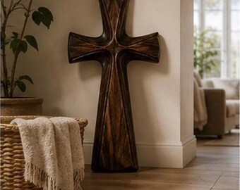 May include: A large, dark brown wooden cross featuring a smooth, polished finish with visible natural wood grain patterns. The cross has a sculpted, contoured design with curved edges that taper toward the center, creating a dimensional appearance.