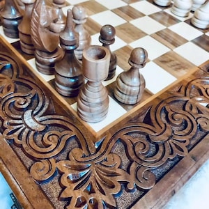 Könnte beinhalten: Ein Schachspiel aus Holz mit aufwendigen Schnitzereien auf dem Brett und den Figuren. Das Schachbrett hat ein helles und dunkles Schachbrettmuster. Die Figuren sind aus dunklem Holz gefertigt und haben eine polierte Oberfläche.