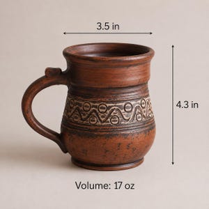 May include: A brown clay mug with a curved handle and a decorative band featuring a repeating geometric pattern. The mug measures 3.5 inches in diameter, 4.3 inches in height, and has a volume of 17 oz as indicated by the text in the image.