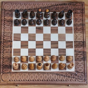 Könnte beinhalten: Ein Schachspiel aus Holz mit aufwendig geschnitzten Bordüren. Das Schachbrett hat abwechselnd helle und dunkle Quadrate, mit Schachfiguren in hellen und dunklen Holztönen. Das Set wird auf einer Holzoberfläche präsentiert.