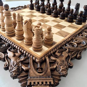 Könnte beinhalten: Ein hölzernes Schachspiel mit einem Brett aus hellen und dunklen Quadraten. Der Rahmen des Brettes ist mit aufwendigen Schnitzereien von Löwenfiguren und geometrischen Motiven verziert. Das Set enthält helle und dunkle Schachfiguren.