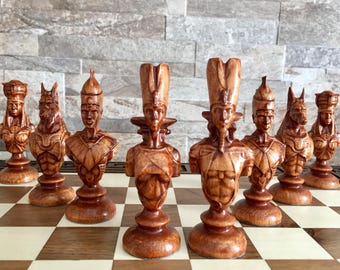 May include: A set of wooden chess pieces with an Egyptian theme. The pieces are carved in the shape of various Egyptian gods and goddesses, including Anubis, Bastet, and Horus. The pieces are painted in a rich brown colour and have a detailed finish.