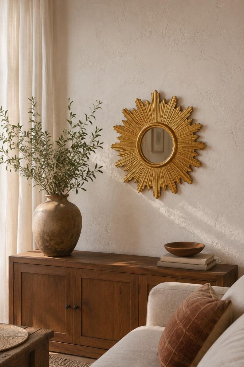 May include: A circular sunburst mirror with a gold-toned frame featuring radiating rays. The mirror has a central reflective glass pane and is mounted on a wall. The design consists of alternating long and short pointed rays extending outward from the center, creating a star-like appearance that serves as a decorative wall accent.