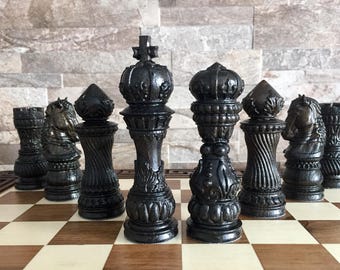 May include: A black chess set with intricately carved pieces on a wooden chessboard. The pieces include a king, queen, bishop, knight, rook, and pawn.