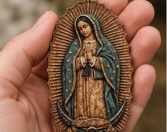 May include: An oval-shaped bronze-toned pendant featuring a relief depiction of the Virgin of Guadalupe. The figure wears a teal mantle with gold stars over a patterned tan robe, with hands clasped in prayer, surrounded by a sunburst and crescent moon.