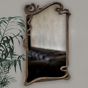 May include: A wooden mirror with an ornate, carved frame. The frame has a flowing, organic design with a dark brown finish.