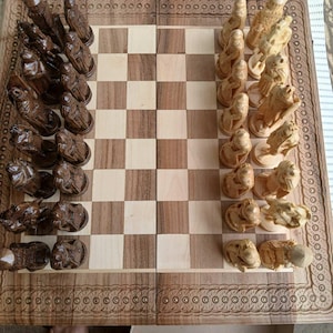 Könnte beinhalten: Ein Schachspiel aus Holz mit aufwendig geschnitzten Figuren mit Tiermotiven. Das Schachbrett hat ein kariertes Muster in hellen und dunklen Holztönen. Die Figuren sind auf dem Brett angeordnet und spielbereit.