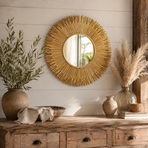 May include: A round wall mirror with a gold sunburst frame featuring numerous thin, radiating metal spikes. The mirror has a circular reflective center and is mounted on a white horizontal plank wall above a wooden dresser.