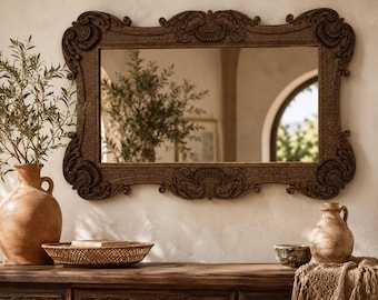 May include: A rectangular wall mirror featuring a dark brown, intricately carved wooden frame with ornate scrollwork and shell-like motifs at the corners and center edges. The reflective glass surface displays a clear view of a room interior.