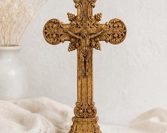 May include: A gold-toned standing crucifix featuring an ornate, detailed cross with intricate scrollwork and grape cluster motifs. The central figure of Jesus is depicted with arms outstretched, mounted on a sturdy, rectangular pedestal base.