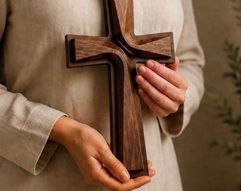 May include: A dark brown wooden cross featuring a layered, dimensional design with carved, curved edges. The cross has a smooth, polished finish that highlights the natural wood grain patterns throughout its structure, creating a deep, rich appearance.