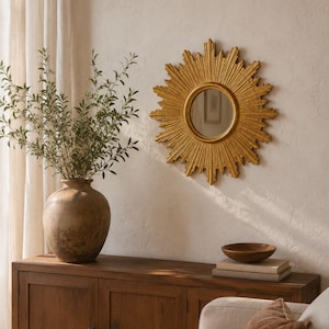 May include: A circular sunburst mirror with a gold-toned frame featuring radiating rays. The mirror has a central reflective glass pane and is mounted on a wall. The design consists of alternating long and short pointed rays extending outward from the center, creating a star-like appearance that serves as a decorative wall accent.