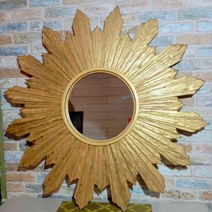 May include: A circular wall mirror featuring a gold-colored frame with a sunburst design. The frame consists of numerous radiating, textured rays of varying lengths that extend outward from the central round glass mirror surface.