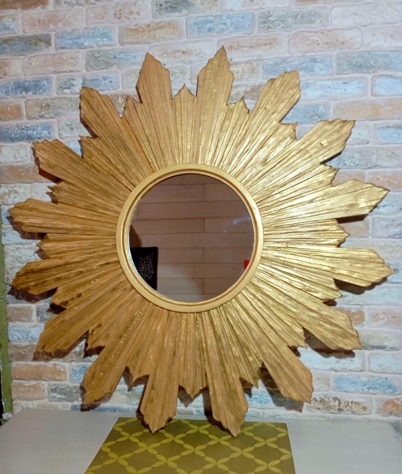 May include: A circular wall mirror featuring a gold-colored frame with a sunburst design. The frame consists of numerous radiating, textured rays of varying lengths that extend outward from the central round glass mirror surface.