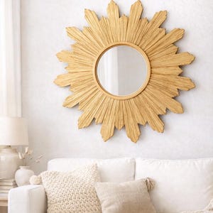 May include: A round wall mirror featuring a decorative sunburst frame with textured, golden-toned rays radiating outward from the central glass. The frame consists of numerous pointed, wooden-like segments arranged in a circular pattern.